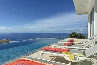 a pool with white lounge chairs and a view of the ocean at Villa OceanAIR by LovelyStay in Prazeres