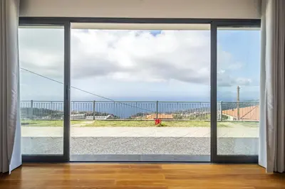an open glass door with a view of the ocean at Faias Haven by Homie in Arco da Calheta