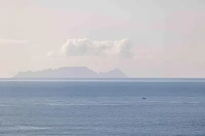 a boat in the water with a mountain in the background at Portinho Mar Apartment in Caniço
