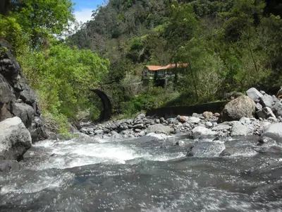 a river with rocks and a house in the background at Moinho do Comandante in Faial