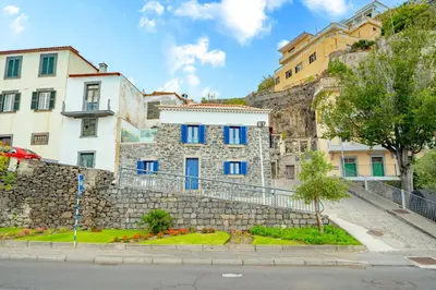 a building with blue windows and a stone wall at Chalé Henrique - Beachfront apartments at Calheta Beach in Calheta