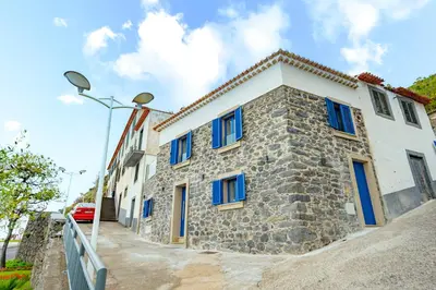 a stone house with blue windows on a street at Chalé Henrique - Beachfront apartments at Calheta Beach in Calheta