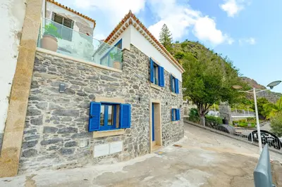 a stone house with blue shutters on a building at Chalé Henrique - Beachfront apartments at Calheta Beach in Calheta