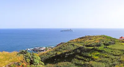 a cruise ship in the ocean next to a hill at Vista Reis Magos in Caniço