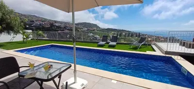 a swimming pool with a table and an umbrella at The Tree of Life House in Ponta do Sol