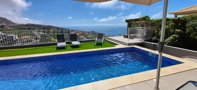 a swimming pool with two chairs and an umbrella at The Tree of Life House in Ponta do Sol