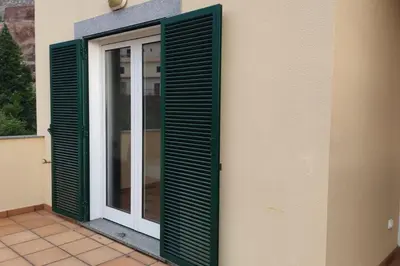 a door with green shutters on the side of a building at Comfy apt in the heart of Ponta do Sol in Ponta do Sol