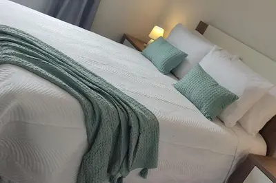 a white bed with pillows and a green blanket on it at Comfy apt in the heart of Ponta do Sol in Ponta do Sol