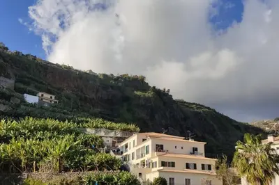 a building on a hill next to a mountain at Comfy apt in the heart of Ponta do Sol in Ponta do Sol