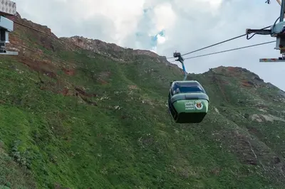 a green gondola flying over a grassy hill at The Mountain View, By OP in São Vicente