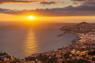 an aerial view of a city with the sun setting over the water at Madeira property in Câmara de Lobos