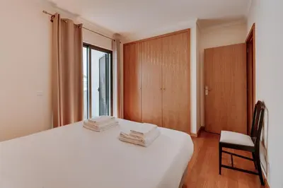 a bedroom with a white bed with a chair and a window at Monumental Lidoview in Funchal