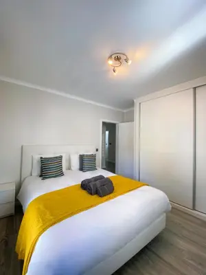 a white bedroom with a large bed with a yellow blanket at Village Square Coastal Apartment 2F in Machico