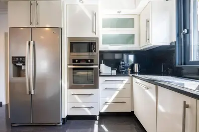a kitchen with white cabinets and a stainless steel refrigerator at Luxury Haven: Heated Pool, AC & Sun in Ponta do Sol