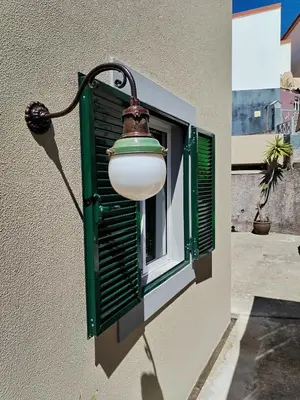 a light on a building with a window with green shutters at Casa do Favinha in Machico