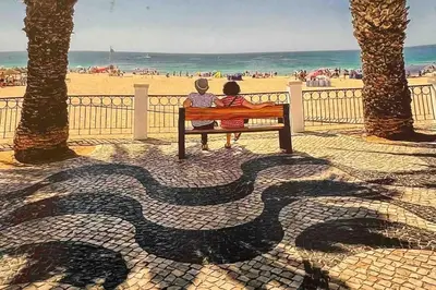 two people sitting on a bench at the beach at Gaivota Ocean view & 5min walk beach in Luz