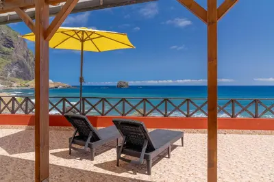 two chairs and a table with a yellow umbrella at Maiata Beach House by Holiday Rental Madeira in Porto da Cruz