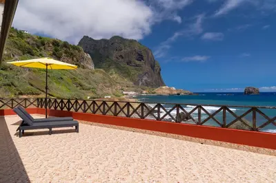 a chair and an umbrella sitting on a beach at Maiata Beach House by Holiday Rental Madeira in Porto da Cruz