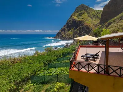 a balcony with a bench and an umbrella and the ocean at Maiata Beach House by Holiday Rental Madeira in Porto da Cruz