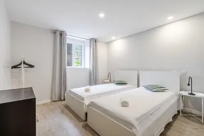 a white bedroom with two beds and a window at JMF House in São Vicente
