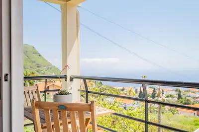 a balcony with a wooden chair and a table with a plant at Casa Flor do Campo in Calheta