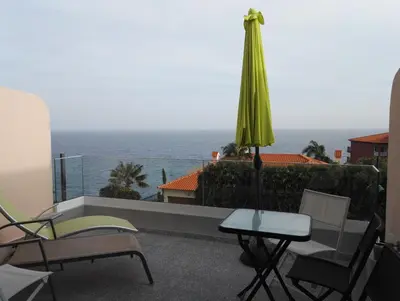 a patio with a table and a green umbrella and the ocean at Ventur Balcony in Caniço