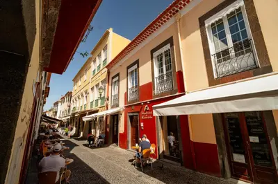 a group of people sitting on a street with buildings at O Cantinho da Mariazinha by Amazing Madeira in Funchal