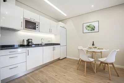 a kitchen with white cabinets and a table and chairs at Casa da Oliveira by Homie in Caniço