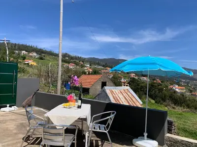a table and chairs with a blue umbrella on a balcony at Casa Jardim Panoramic View in Estreito da Calheta