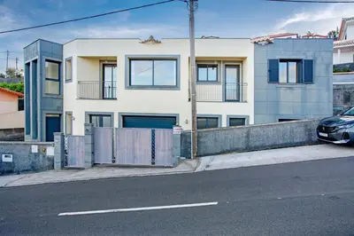 a white house with a fence and a car parked on a street at Casa da Bemposta in Machico