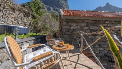 a patio with a table and chairs on a stone wall at Stonewood Valley by LovelyStay in Curral das Freiras