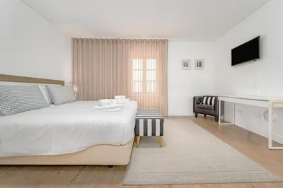 a white bedroom with a bed and a desk at Studios Funchal in Funchal
