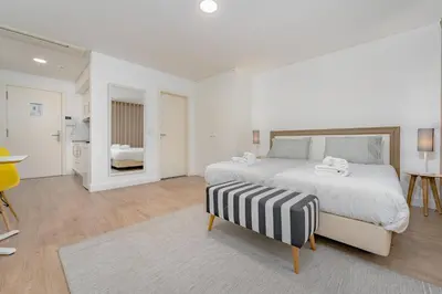 a white bedroom with a large bed and a table at Studios Funchal in Funchal