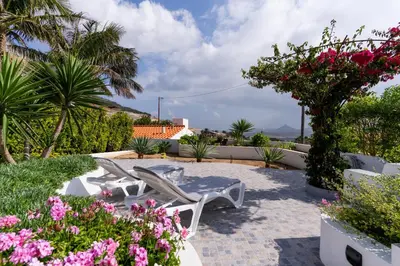 a patio with two white chairs and flowers at Casa das Malvas in Porto Santo