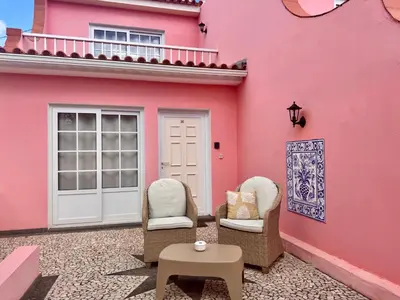 a pink house with two chairs and a table at Falesia Gardens in Caniço