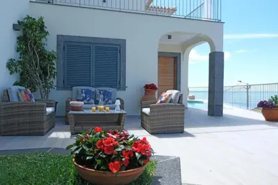 a patio with chairs and a table and flowers at Ocean escape with private pool in Arco da Calheta