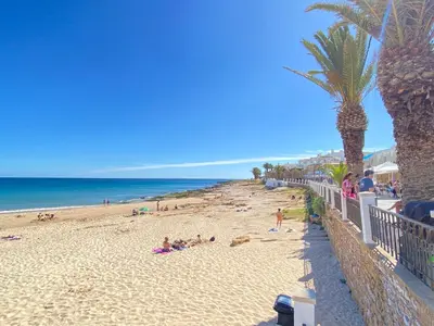 a beach with people laying on the sand and palm trees at NEW Luztur apartment 3min from Luz Beach in Luz