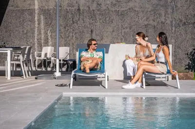two people sitting in lawn chairs next to a swimming pool at Villa Elysian Oasis by Homie in Fajã da Ovelha