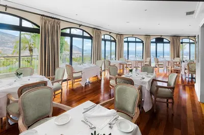 a restaurant with white tables and chairs and windows at Quinta Funchal Gardens - Adults Only in Funchal