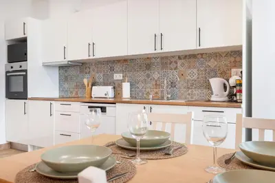 a kitchen with white cabinets and a wooden table with wine glasses at Casa Cintra in Almádena