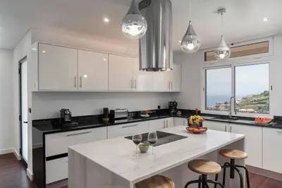 a kitchen with white cabinets and a island with bar stools at Casa das Maravilhas by An Island Apart in Câmara de Lobos