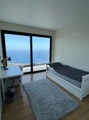 a bedroom with a bed and a desk and large windows at Villa Arco Iris in Arco da Calheta
