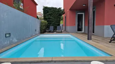 a large blue swimming pool next to a red building at The Red Hot Chill House by LovelyStay in Arco da Calheta