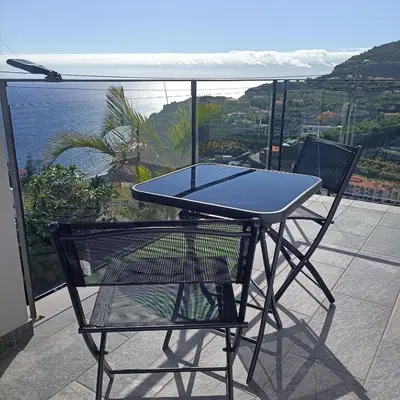 a table and chair on a balcony with a view of the ocean at Gertrudes Dream House in Ponta do Sol