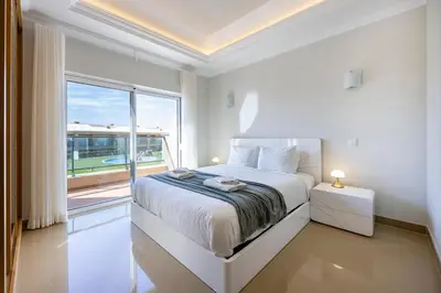 a white bedroom with a bed and a large window at Boa Vista - Casa Jacques in Lagos