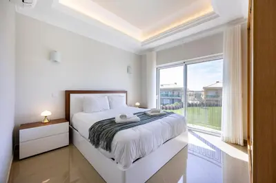 a white bedroom with a bed and a large window at Boa Vista - Casa Jacques in Lagos