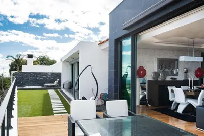 an outdoor patio with a glass table and white chairs at Casa Refúgio dos Canhas in Ponta do Sol