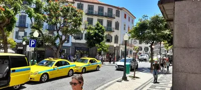 a woman walking down a city street with yellow taxis at RC Fltas Funchal B in Funchal