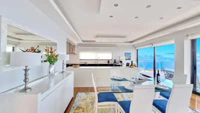 a white kitchen with a glass table and chairs at Azure Serenity Villa by LovelyStay in Santa Cruz