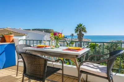 a table on the balcony with a view of the ocean at Casa dos Zefiros in Luz